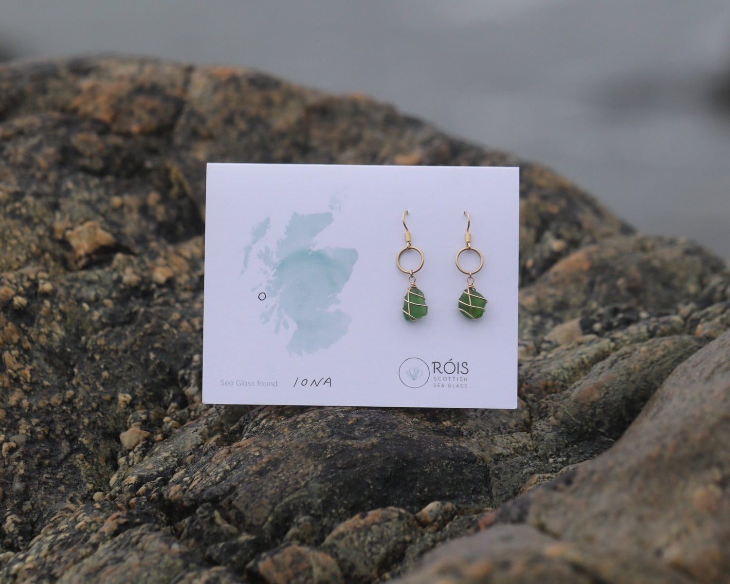 Pair of earrings on a card against a textured stone background